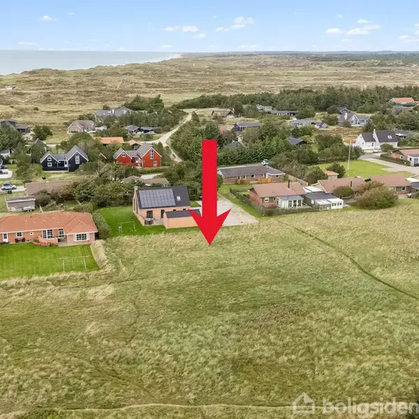 En stor, rød pil peger på et hus midt i et beboelsesområde med flere huse omkring, omgivet af marker og skove. Kysten ses i baggrunden.