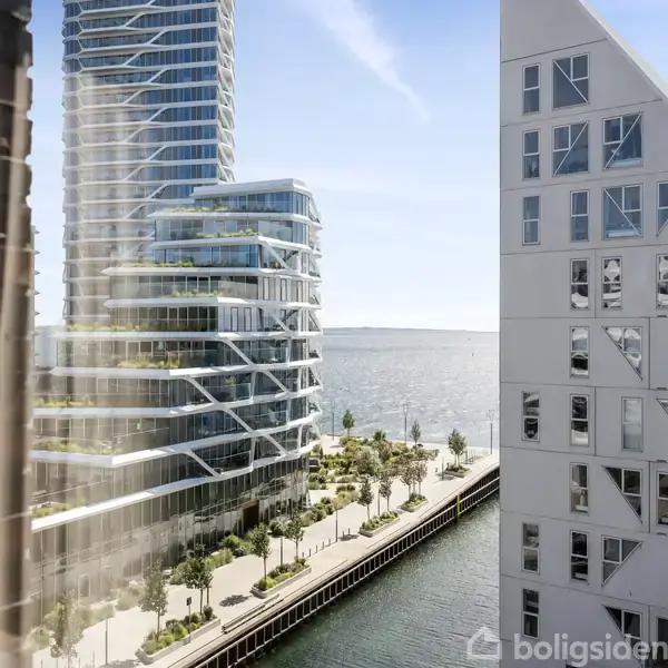 Moderne højhuse står langs en kanal, med træer plantet på promenaden. En stor bygning til højre har geometriske vinduer. I baggrunden ses vandet og en klar himmel.