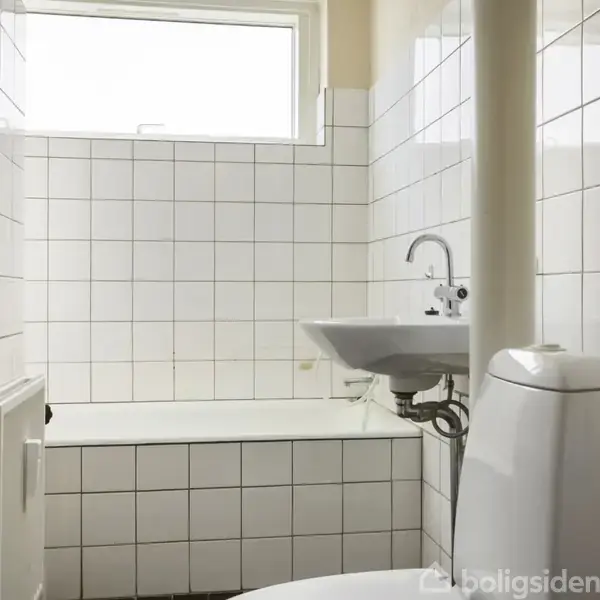 En hvid flisebelagt badeværelse med en vask og et toilet modsat et badekar. Et lille vindue i toppen tillader naturligt lys at strømme ind.