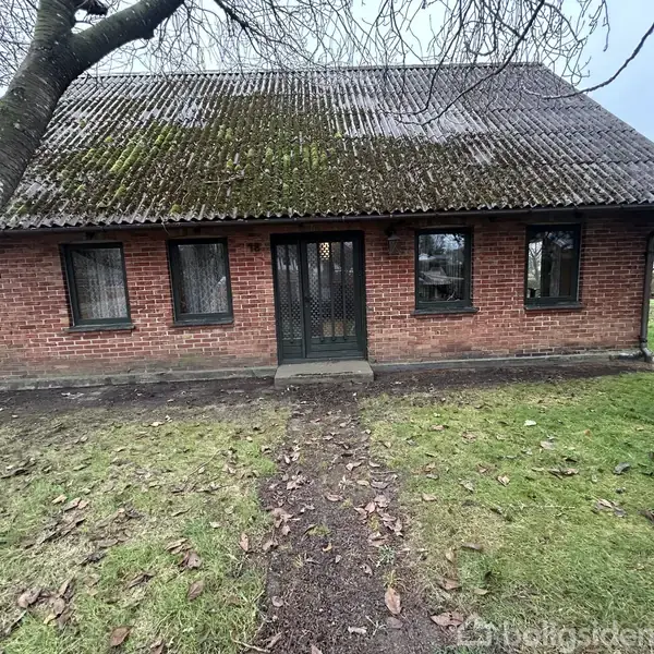 Et rødt murstenshus står stille med en sort trædør og fire vinduer, omgivet af en grøn græsplæne og et bar træ i forgrunden.