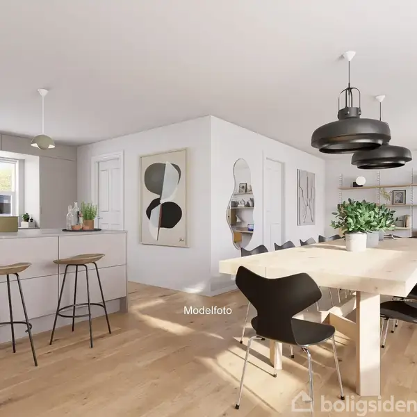 Køkken-alrum med langt spisebord. Sorte stole og moderne lamper hænger over bordet. Store vinduer giver naturligt lys. Køkkenø med barstole, træ og hvide overflader. Tekst: “Modelfoto”.