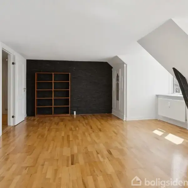 Et tomt rum med trægulv har en mørk bogreol op ad en sort væg. Hvide vægge har teksten: "Too many of us are not living our dreams be...". Store vinduer giver lysindfald.