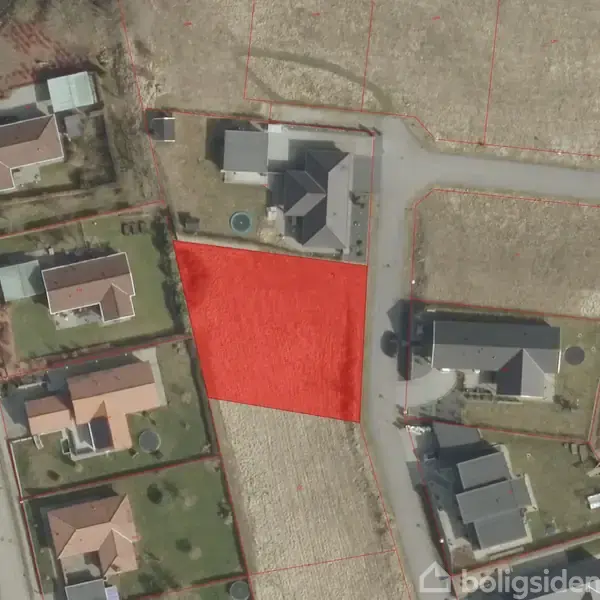 En rødmarkeret grund ses fra oven, omgivet af huse langs en vej. Grunden er tom, mens de omkringliggende huse har haver og indkørsler.