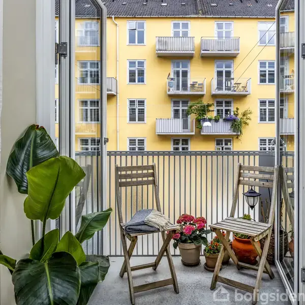 En træbakke med en flaske fra Meraki og en kop står på kanten af et badekar. Badeværelset har hvide fliser og en sølvfarvet vandhane.