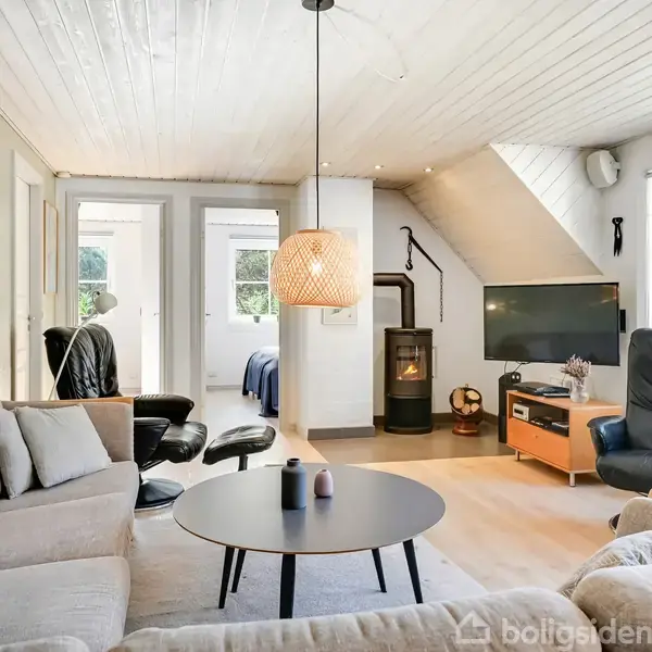 Spisebord med otte stole står midt i et lyst rum med store vinduer mod haven. Lamper hænger over bordet, og en lille dansk flag dekoration står på bordet.