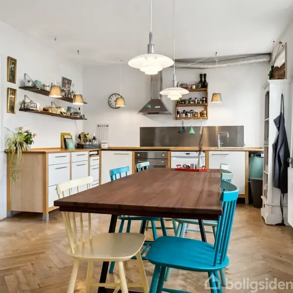 Et træbord med farverige stole står i et lyst køkken. Køkkenet har åbne hylder, vægure, planter og en stor køleskab i rustfrit stål. Rummets indretning er moderne og funktionelt.