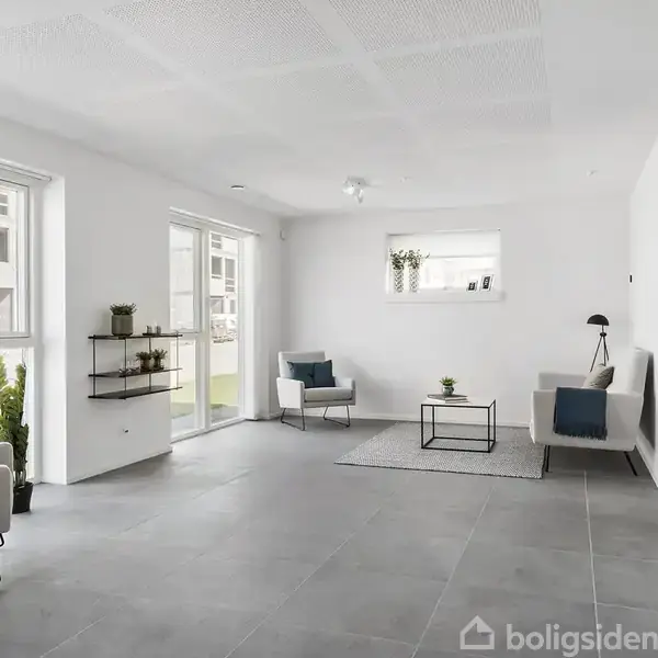 Stue indrettet med to stole og et lille bord på et gulvtæppe. Hylder med planter hænger på væggen. Store vinduer og lysegrå flisegulv dominerer omgivelserne.