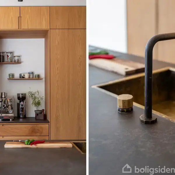 Trækøkkenskab med indbygget kaffeudstyr og hylder til krus; ved siden af er en mørk køkkenbordplade med sort vandhane og vask. Grøn plante i forgrunden.