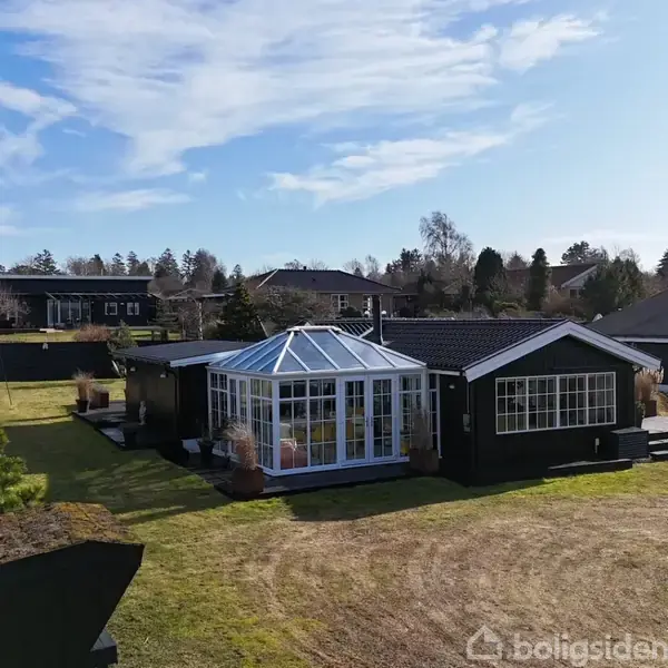 Et spisebord med sorte overflader og gule stole står i en lys havestue. Udenfor ses en velholdt have og et gråt anneks. Bordet er pyntet med dekorative genstande.