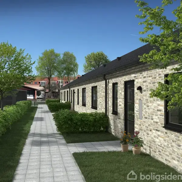 En række af moderne rækkehuse med murstensfacade står langs en flisebelagt sti. Omkring dem er der grønne hække, træer og buske under en lys, blå himmel.