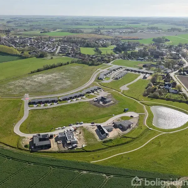 Byggeri i fremdrift, hvor flere huse er under opførelse på et nyanlagt boligområde. Landskabet omkring består af marker og en by i horisonten.