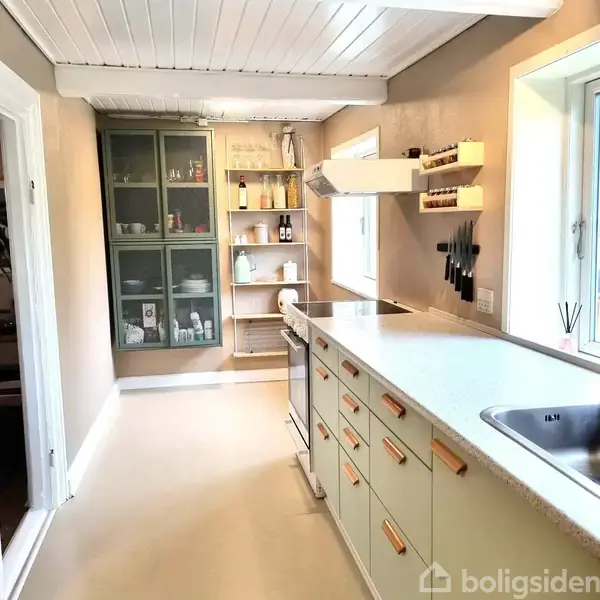 En trætrappe stiger opad ved siden af en hvid dør. Væggene er beige, og gulvet er af træplanker. Loftet har hvidmalede paneler. Ingen tekst synlig.