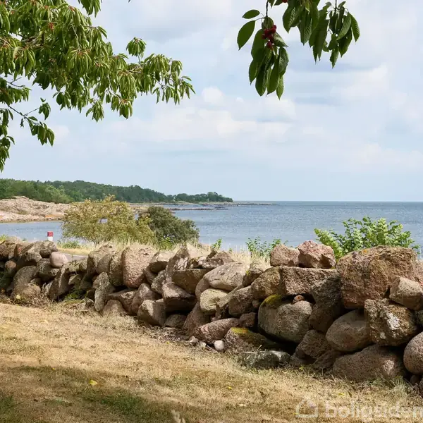 Bindingsværkshus med rødt tegltag står i en frodig have nær kysten. En flagstang står i forgrunden, og havet kan ses i baggrunden.