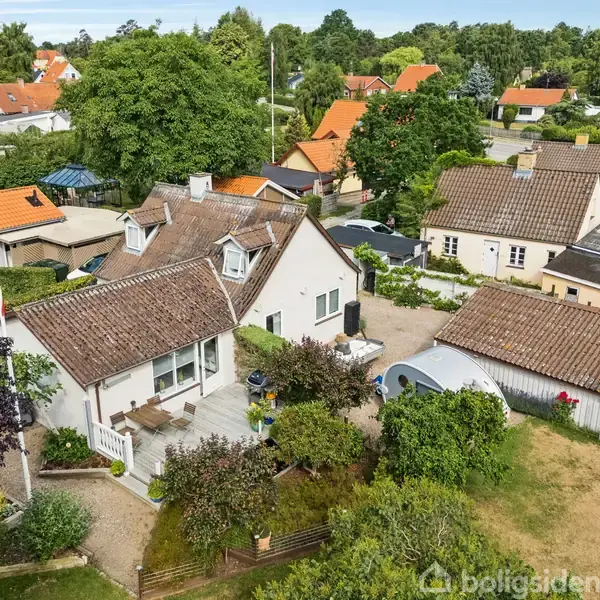 Hus med rødt tegltag står i en frodig have med flagstang. Omkringliggende villaer ses i et grønt boligkvarter.