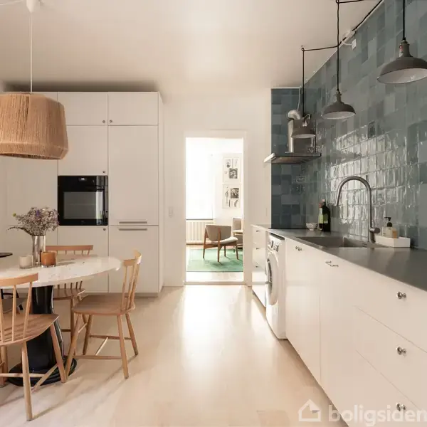 En moderne stue har en stor, grå sofa og rundt sofabord. Store vinduer lader lys strømme ind. Der er en sort gulvlampe og farverigt kunstmaleri på væggen. Ingen tekst fundet.