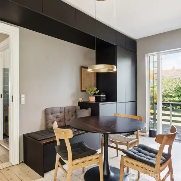 Et spisebord med fire stole står i et lyst rum. En lampe hænger over bordet. Der er en bænk ved siden af bordet og en åben dør til en altan med udsigt.