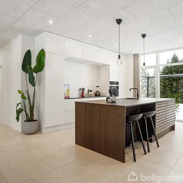 Et moderne murstenshus står stille i et velplejet haveområde med græs og planter. Husnummeret "28" er synligt på bygningen.