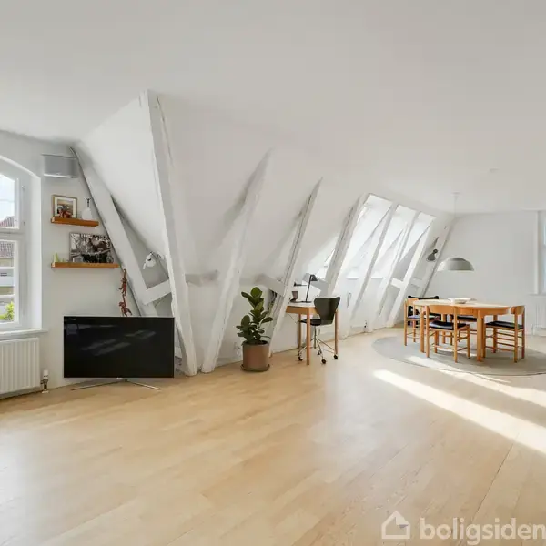Gul bygning med kamtakkede gavle står stille omgivet af velplejede hække og flisebelagt sti. Skyfri blå himmel i baggrunden, hvilket skaber en rolig boligscene.