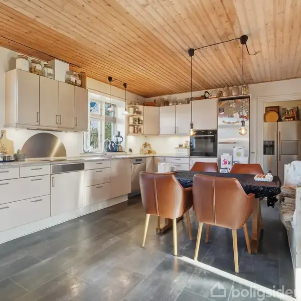 En have med højbede indeholder forskellige planter, der vokser i rækker. Hegn omkranser bedene. Træer omkranser området, og et hus er synligt til venstre.