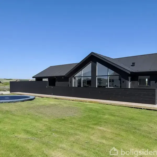 Sort moderne hus med store vinduer står stille på en grøn græsplæne. En rund, nedgravet pool er placeret i nærheden. Klar blå himmel ses i baggrunden.