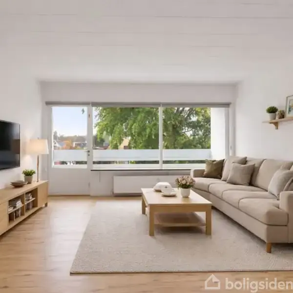 En beige sofa står langs en væg med puder, mens et træbord foran holder dekorationer; en medieenhed med planter og en TV-skærm er til venstre. Store vinduer giver udsigt til træer.