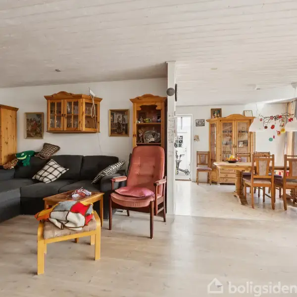 Stue med sort hjørnesofa, et sofabord med bøger og tæpper, og en rød stol. Kontekst: spisebord og stole i lyst rum med store vinduer og skænke.