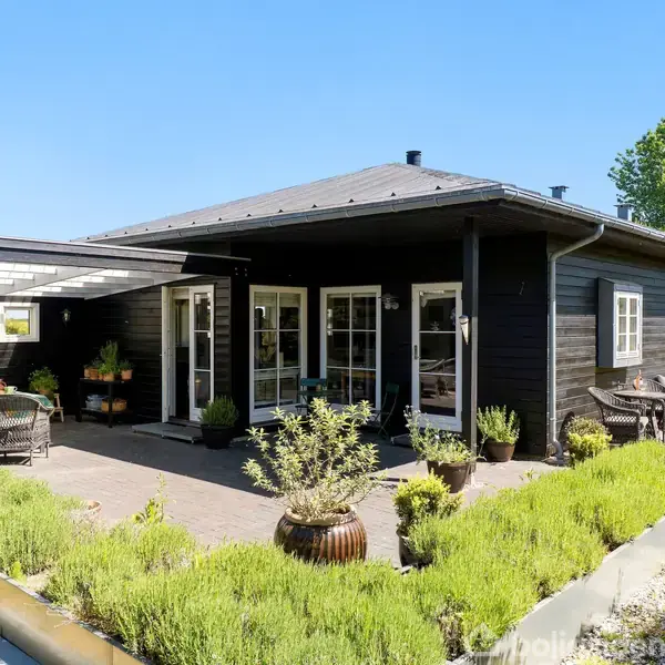 Gråt køkken med moderne skabe og integreret ovn; grønne stribede tæpper på trægulv; grøn stol og et bord i baggrunden ved siden af en brændeovn.