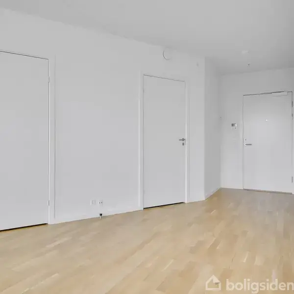 To hvide døre står på en hvid væg i et rum med lyst trægulv, der giver et rent og minimalistisk indtryk.