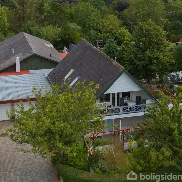 To huse ses ved siden af hinanden, omgivet af frodige træer og grønne områder. De adskilles af en flisebelagt indkørsel og er beliggende i en skovrig, fredelig forstad.