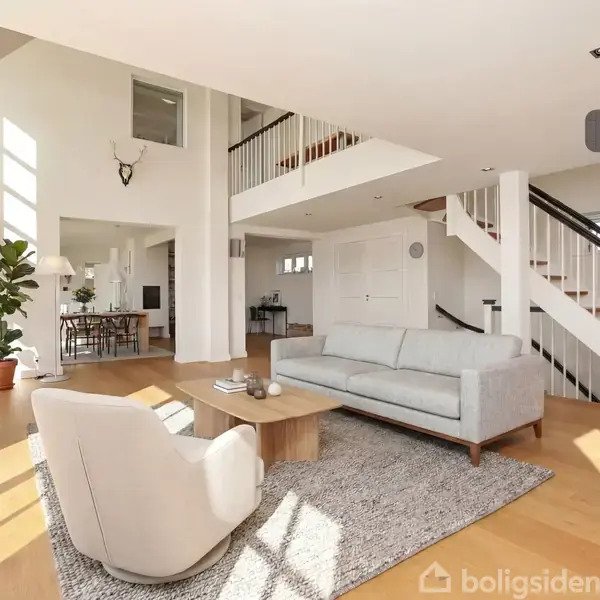 Lys, moderne stue med lyse møbler. En sofa og stol står på et tæppe ved et sofabord. Trappe til højre, spisestue i baggrunden og grøn plante ved vinduet. Tekst: "Visualisering".