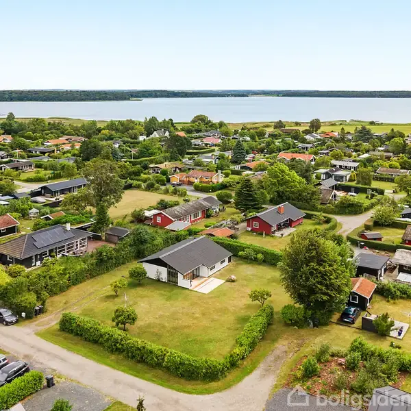 Huse ligger spredt i en grøn landsby nær en sø i baggrunden. Veje adskiller haverne og træerne i det frodige landskab.
