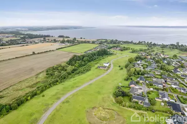 Landsbyhuse står stille i et grønt landskab ved en bugt med marker og skove i baggrunden.