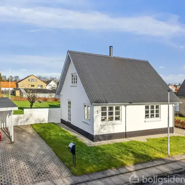 Et hvidt hus med sort tag står på en velholdt græsplæne. Til venstre holder en rød bil i en overdækket carport. Solrig dag, rolige omgivelser. Huset har nummer 31.