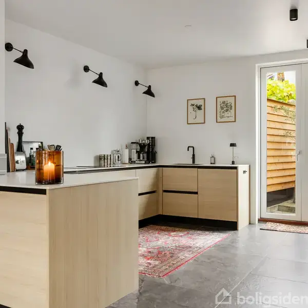 Et moderne køkken med lyse træskabe og sort bordplade. En kande står på øen, omgivet af lamper og dekorationer. Store glasdøre fører ud til en hyggelig gårdhave.