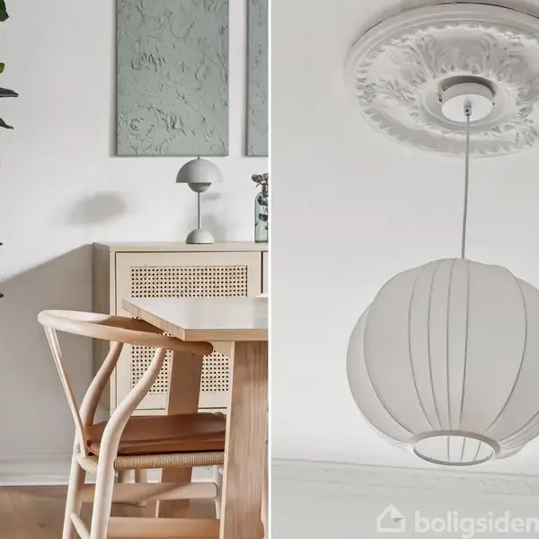 En stue med en træstol og et bord ved siden af en plante i kurv. En hængende, hvid lampe med detaljeret loftroset. Rolig og lys indretning.