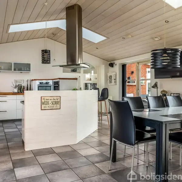 Køkken i åbent rum med sort spisebord og stole. Rummeligt og moderne design med opvaskemaskine og ovn. Skilt på køkkenøen: "Dinner choices: 1. Take it 2. Leave it 3. WEX - SORRY".