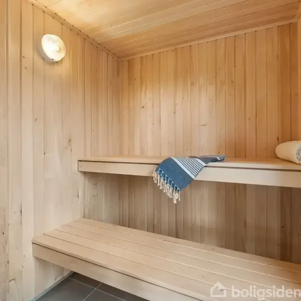 Sauna med trævægge og -bænke; to håndklæder er placeret på bænken, et foldet og et udrullet. Et opvarmningsaggregat med sten står i venstre side.