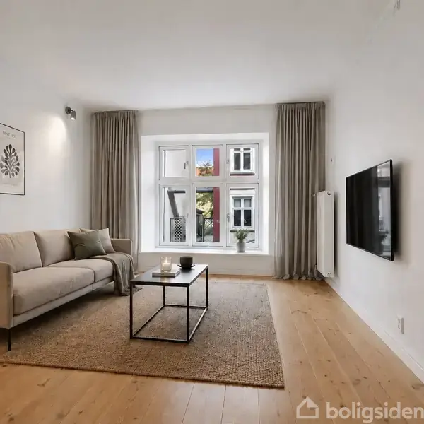 Stue med sofa til venstre, sofabord i midten på et tæppe, fladskærm på væggen til højre. Store vinduer med gardiner skaber lysindfald, træplankegulv og et vægmaleri.