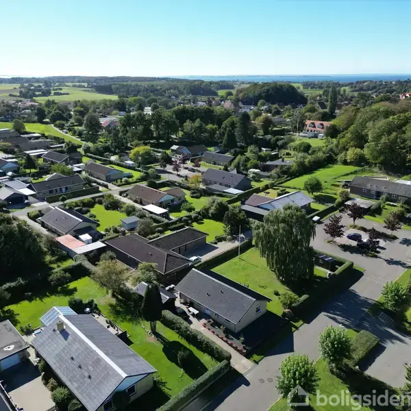 Huse breder sig ud i et roligt boligområde omgivet af frodige træer og velplejede græsplæner, overset af en klar himmel.