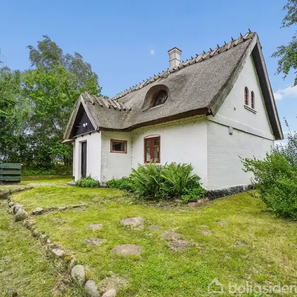 Stråtækt hus står stille omgivet af en frodig have med græs og buske. Huset har hvide mure, røde vinduer og en skorsten. Træer og en lys himmel ses i baggrunden.