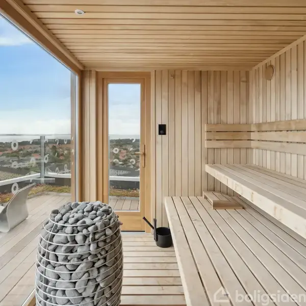 Sauna med træbænke og lavasten, står stille. Den er placeret ved en glasvæg, som giver udsigt over byen og bagved ligger en balkon med moderne stole.