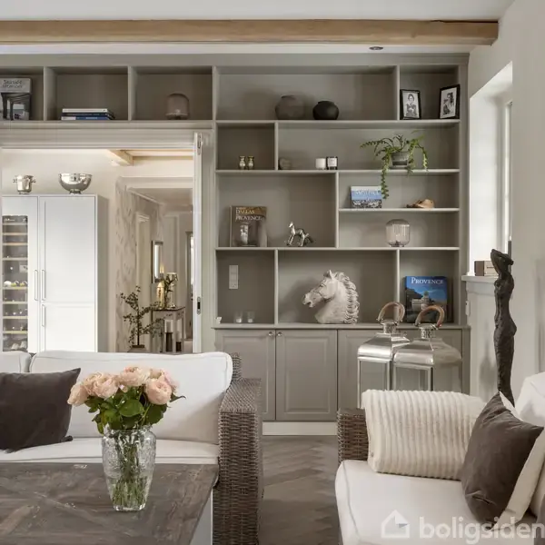 En stue med grå reoler fyldt med bøger og dekorationer, en hvid sofa med pude, og et træsofabord med en vase med roser, skaber en stilfuld, hyggelig atmosfære.