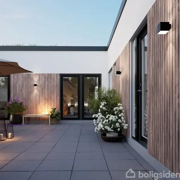 Terrasse med moderne møbler og planter oplyst af bløde lamper om aftenen. Trævægge og store vinduer omkranser området, og der ses et parasol samt blomstrende potteplanter.