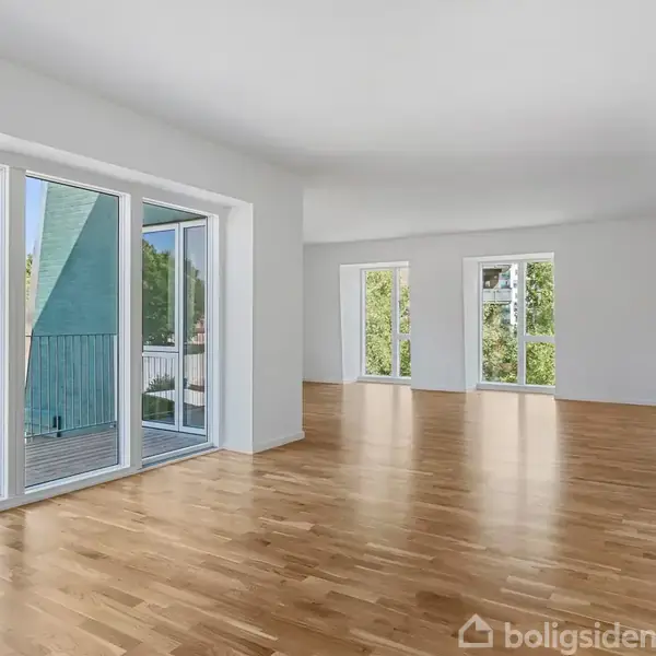 Lyst stueområde med trægulve strækker sig mod store vinduer og altandøre, der åbner ud til en balkon; udenfor ses bygninger og grønne træer.