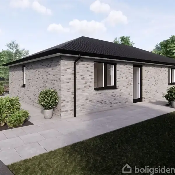 Et moderne hus står stille på en flisebelagt terrasse. Det har grå mursten, mørkt tag, og omgives af græsplæne med buske. Skov kan ses i baggrunden.
