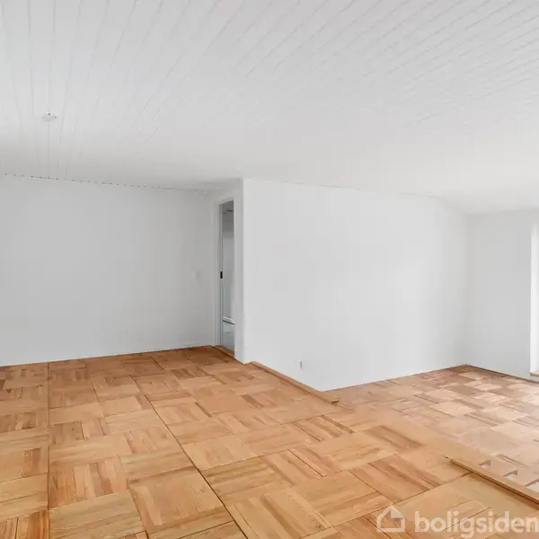 Et lyst rum med trægulv, enkelt vindue og dør, der åbner ud til en have. Væggene er hvide, og der er en radiator under vinduet.