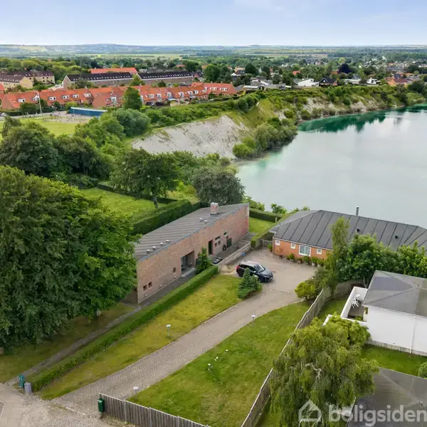 Lang, smal køkken med sorte skabe og hvide bordplader. En rød orientalsk løber ligger på gulvet. Blå lampe hænger over vasken. Lysindfald fra små vinduer.