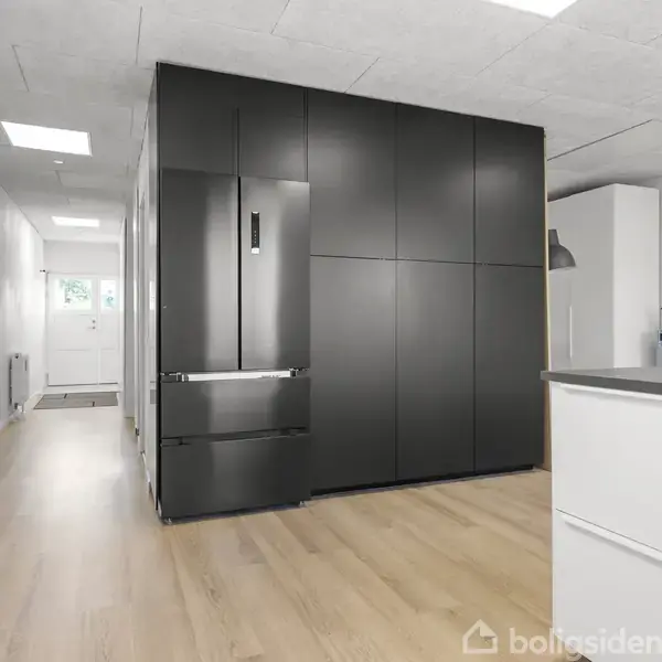 Et køkken med et sort køleskab integreret i en skabsvæg. Trægulve og hvidmalede vægge omgiver rummet, der har et moderne, minimalistisk design.
