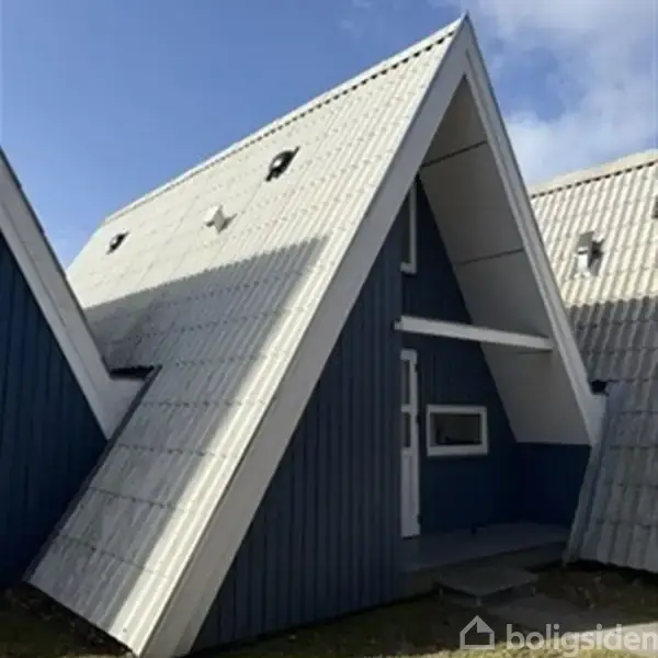 Et A-formet hus med blå facade og hvidt tag er synligt. Husets skrå tagflader mødes, og en lille dør samt et vindue ses på den øverste etage.