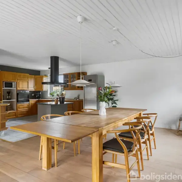 En hjørnesofa med grå og gule puder står i en stue. På sofabordet er en vase med blomster. Der hænger en lampe over bordet ved en mørkegrå væg.